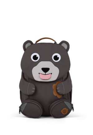 Dunkelgrauer Kinderrucksack in Bärchenform mit großen Augen, herausgestreckter rosa Zunge, hält eine kleine braune Blume und hat einen Tragegriff oben.