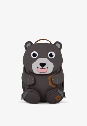 Children’s dark gray bear-shaped backpack with large eyes, pink tongue sticking out, holding a small brown flower, with a carry handle on top.