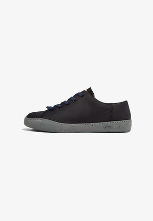 Svart sneaker med en texturerad ovandel, som har blå snören, en fläckig grå sula och kontrasterande sömmar längs kanterna.