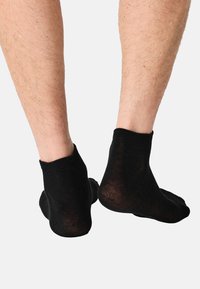 Sorte ankelstrømper lavet af et blødt, elastisk materiale. Designet har en ribbet kant og en glat tekstur med en ugennemsigtig finish.