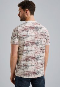 Kortærmet T-shirt i beige med et tekstureret abstrakt mønster med røde og sorte accenter. Fremstillet af blødt stof med design i rund hals.
