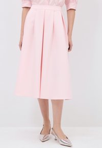 Gonna midi plissettata rosa realizzata in tessuto liscio, con vita aderente e silhouette fluida. Abbinata a scarpe slingback argentate.