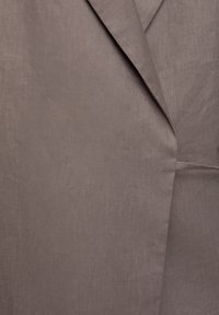 Gros plan sur un tissu en lin taupe avec un détail de revers plié, montrant la texture et les coutures d'un vêtement sur mesure.
