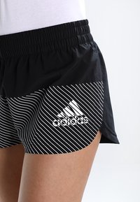 Svarta idrottsshorts med vita diagonala ränder, elastisk midja och en vit logotyp på nedre vänstra sidan. Lättviktig tyg.