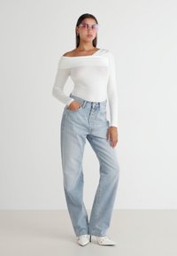 Witte off-the-shoulder blouse met lange mouwen, lichtblauwe hoge taille jeans en puntige witte hakken. Accessoires zijn roze zonnebril.