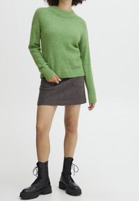 Green wool sweater with a round neck, paired with a gray felt mini skirt and black lace-up combat boots.