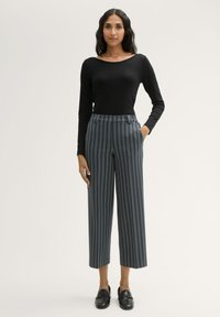 Zwarte lange mouw top gecombineerd met blauwwitte geruite wijde broek met hoge taille, zijzakken en een gestructureerd patroon. Zwarte instappers maken de look compleet.