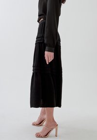 Gonna midi nera a strati realizzata in tessuto leggero, con pannelli orizzontali e una silhouette fluida. Abbinata a sandali con tacco color nude.