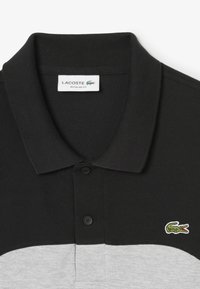 Mustapungentti polo-paita, jossa on tekstuuri, kahden napin kaulukset ja vihreä krokotiili-logo vasemmassa rinnassa.