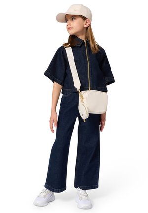 Top court en denim à manches courtes avec fermeture éclair, associé à un jean large. Baskets blanches et sac bandoulière crème avec des accents dorés.