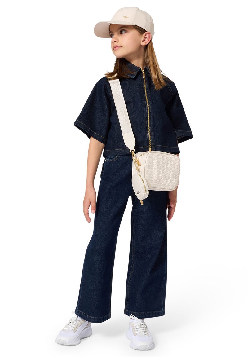 Top court en denim à manches courtes avec fermeture éclair, associé à un jean large. Baskets blanches et sac bandoulière crème avec des accents dorés.