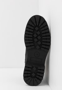 Semelle en caoutchouc noir avec des rainures profondes et des motifs, présentant des formes croisées et un logo circulaire. Conçue pour l'adhérence et la durabilité. Taille 42.