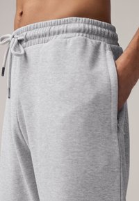 Gray cotton joggers with an elastic waistband, drawstring, and side pockets; textured fabric with a soft finish and minimal stitching details.