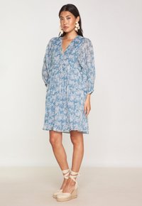 Abito floreale azzurro chiaro con scollatura a V profonda, maniche lunghe trasparenti e vita arricciata. Indossato con zeppe in espadrilles beige.