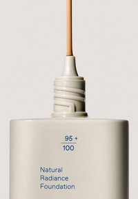 Natural Radiance Foundation i en mat hvid flaske med blå tekst, der har et slankt mundstykke med en lys beige foundation nuance.