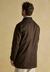Brązowy wodoodporny płaszcz o dopasowanym kroju, z długimi rękawami i wentylacją z tyłu, z wysokim kołnierzem i guzikami przy mankietach.