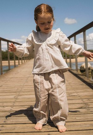 Mlad otrok v bež oblačilih v vintage slogu hodi bos po leseni poti pod jasnim nebom.