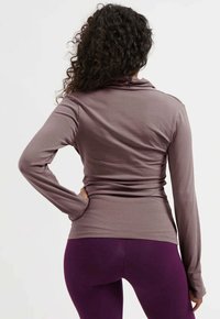 Brauner langärmeliger Oberteil mit einer figurbetonten Silhouette, ausgestattet mit einem Schalkragen und glatter Textur, kombiniert mit lila Leggings.