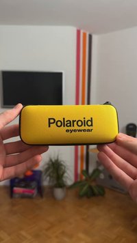 Κίτρινη υφασμάτινη θήκη γυαλιών με μαύρο φερμουάρ και λογότυπο "Polaroid eyewear". Ορθογώνιο σχήμα με υφή στην επιφάνεια και στρογγυλεμένες άκρες.