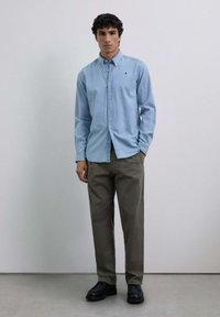 Lichtblauwe overhemd met lange mouwen en een kraag, gecombineerd met olijfgroene broeken en zwarte schoenen. Eenvoudig ontwerp, geen patronen of accenten.