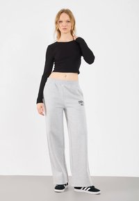 Zwart crop-top met lange mouwen gecombineerd met grijze sweatpants met wijde pijpen, bedrukt met "TOKYO 1991" aan de voorkant. Zwarte sneakers maken de outfit compleet.