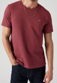 Burgundin värinen puuvillapaita lyhyillä hihoilla. Rinnassa on pieni punainen Levi's-logo. Sileä pinta; yhdistettynä tummansiniset farkut.