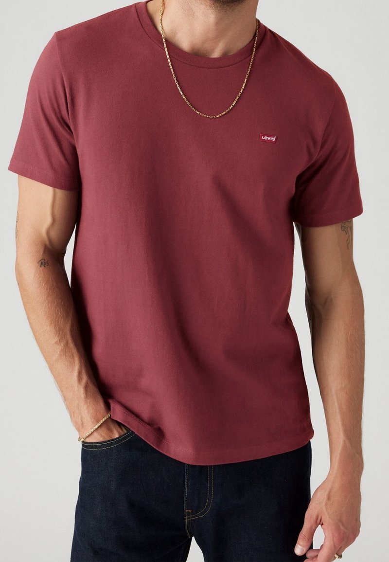 Burgundin värinen puuvillapaita lyhyillä hihoilla. Rinnassa on pieni punainen Levi's-logo. Sileä pinta; yhdistettynä tummansiniset farkut.