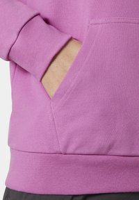 Sudadera rosa con tejido texturizado, que cuenta con un bolsillo frontal y puños y dobladillo acanalados. Los detalles de costura añaden estructura al diseño.