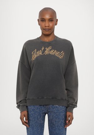 Grå hettegenser med ribbede kanter og ermer, med gullfarget tekst "Just Sweat." Parret med glitrende blå jeans.