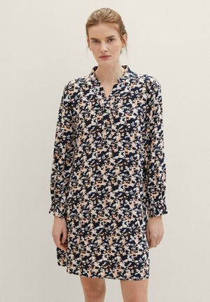 Robe fleurie avec une base bleu marine foncé, ornée de fleurs pêches et blanches. Manches longues avec des poignets élastiques et un col en V, longueur mi-cuisse.