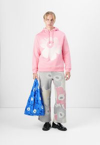Rosa Kapuzenpullover mit großem weißen Blumenmuster, graue gemusterte Jogginghose und blaue Blumenhandtasche. Schwarze Schuhe vervollständigen das Outfit.
