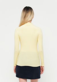 Langarm, ribbel top in zacht geel met een gegolfde halslijn en slim fit, gecombineerd met een donkerblauwe rok.