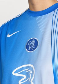 Nike sininen jalkapallopaita sisältää pyöreän Chelsea FC -logon ja valkoisen swooshin, sekä gradienttisuunnittelun ja tekstuurikankaan.
