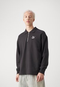 Zwarte rits polo sweatshirt met lange mouwen en geribde manchetten, voorzien van een wit logo op de linkerkant van de borst. Glad stoftextuur.