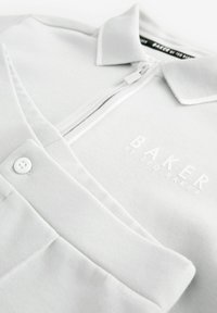 Světle šedá polokošile se zipovým uzávěrem, ribovaným límcem a diskrétně vyšitým logem "BAKER by TED BAKER" v bílé barvě. Měkká texturovaná tkanina.