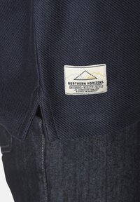 Marineblaue Textilie mit Fischgrätenmuster, mit einem cremefarbenen Etikett, das Berge und den Text "NORTHERN HORIZONS" in der unteren rechten Ecke zeigt.