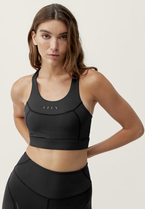 Čierny športový podprsenka s dizajnom na preteky, priliehavým strihom a textúrovanou tkaninou. Obsahuje jemné detaily loga značky v prednej časti.