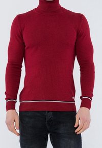 Czerwony sweter z golfem, wykonany z dzianiny, o dopasowanym kroju, z prążkowanymi mankietami i kontrastowym białym i czarnym paskiem na dole.