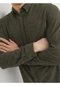 Camicia button-down verde scuro realizzata in tessuto testurizzato, con taschino sul petto e maniche arrotolate con bottoni marroni.