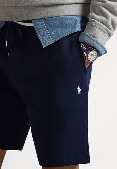 Granatowe bawełniane spodenki z bocznymi kieszeniami, z małym białym haftowanym logo i sznurkiem w talii. Noszone z szarą bluzą i dżinsową koszulą.