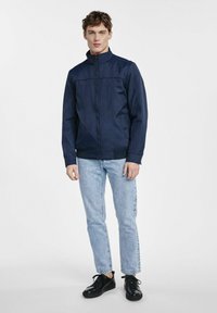 Granatowa, lekka kurtka z wysokim kołnierzem, zapinana na zamek błyskawiczny z przodu i bocznymi kieszeniami. Połączona z jasnoniebieskimi dżinsami i czarnymi butami typu lace-up.