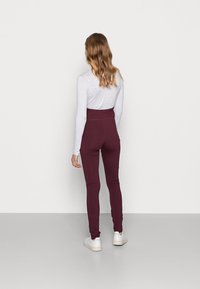 Maroon high-waisted leggings made of stretchy material, paired with a light gray long-sleeve top and white sneakers. Smooth texture.