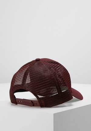 Bordeauxrød mesh trucker-kasket med justerbar snapback-rem vist på en hvid pedestal mod en ensfarvet lysegrå baggrund.