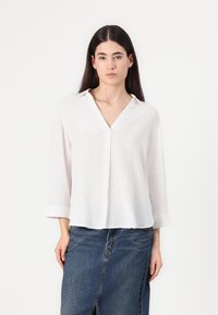 Blusa bianca in lino con scollo a V e maniche a tre quarti, caratterizzata da una vestibilità comoda e una morbida texture, abbinata a una gonna di denim.