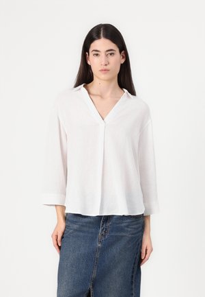 Blusa bianca in lino con scollo a V e maniche a tre quarti, caratterizzata da una vestibilità comoda e una morbida texture, abbinata a una gonna di denim.