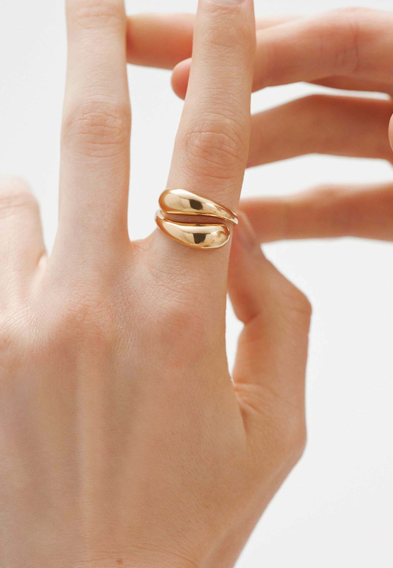 Anillo en tono dorado con un diseño tubular suave y dos bandas entrelazadas. La superficie está pulida para un acabado reflectante.