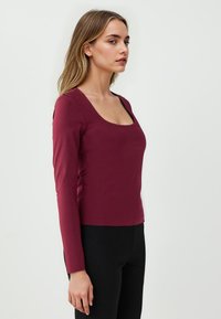 Maglietta bordeaux a maniche lunghe con scollatura quadrata e design aderente. Realizzata in tessuto morbido; fessure laterali all'orlo per facilitare i movimenti.