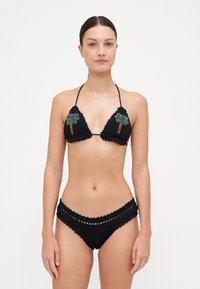 Melna tamborēta bikini komplekts, kurā ir trīsstūrveida tops ar izšūtām ziedu apdare un zemu vidukli ar viļņotām malām un izgriezumiem.