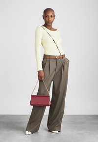 Raitareun kevyt keltainen pitkähiha, muotoiltu ruskea housut, valkoiset kärjetään kengät ja viininpunainen olkalaukku ketjuhihnalla.