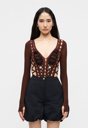 Καφέ πλεκτό κορμάκι με βαθύ V-λαιμό, ανοίγματα στα πλάγια και λεπτομέρειες με μαύρα κορδόνια. Συνδυάζεται με μαύρο σορτς ψηλής μέσης με βολάν στο τελείωμα.